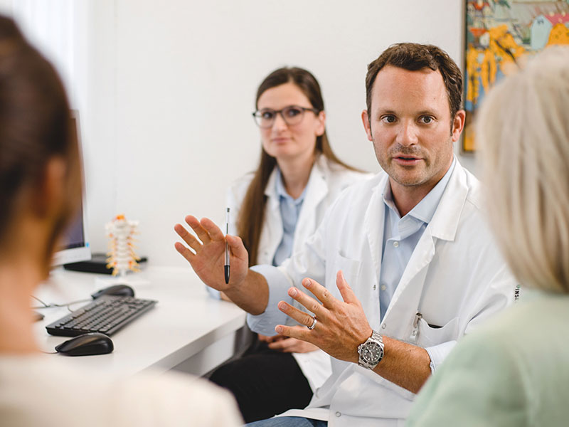 Photo of 2 doctors explaining something to a patient and another woman.