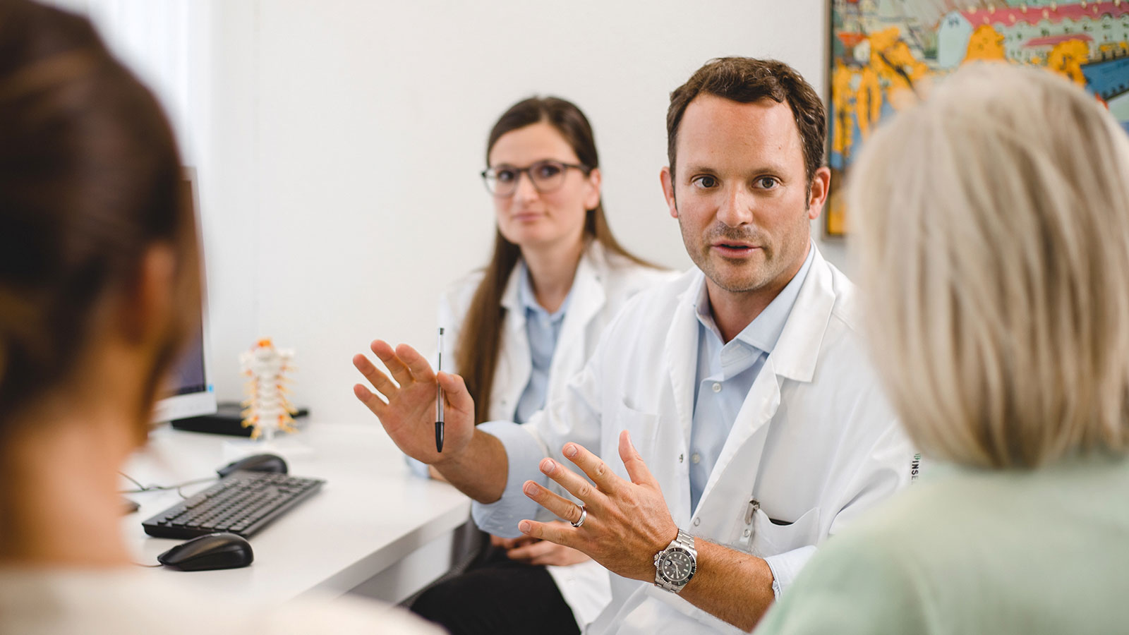 [Translate to Français:] Ein Arzt und eine Ärztin besprechen mit der Patientin, die in Begleitung ihrer Tochter ist, Diagnose und Therapie.